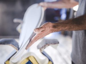 Craftsman shaping a white surfboard by hand