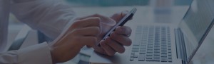 Hands holding smartphone above laptop keyboard