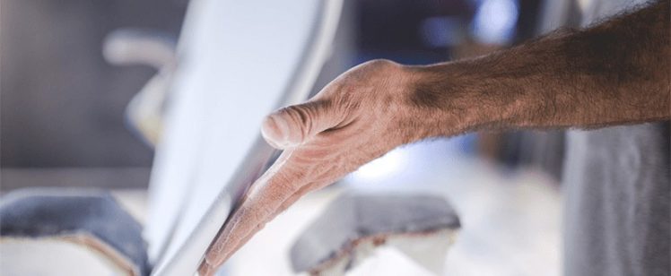 Craftsman shaping a white surfboard by hand