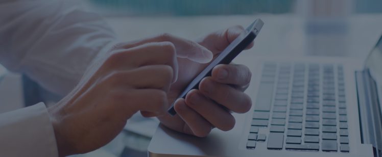Hands holding smartphone above laptop keyboard