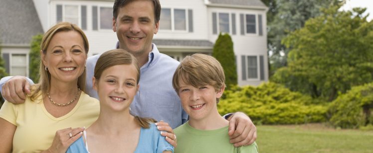 Smiling family of four in front of house